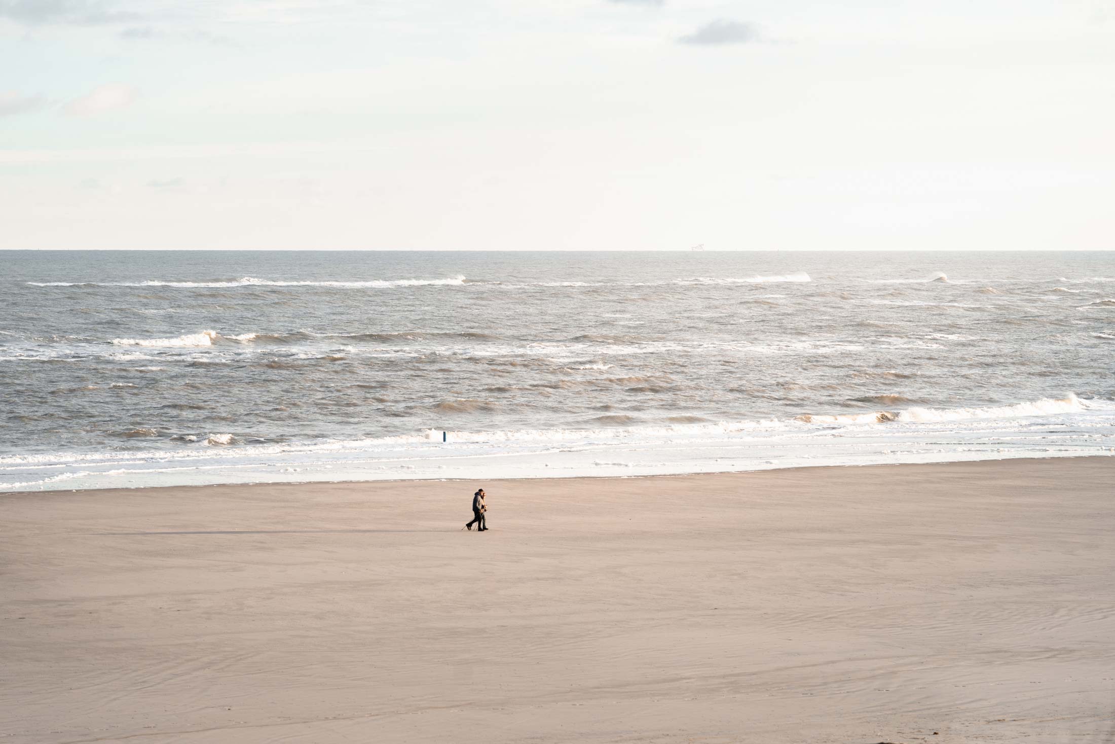 Weitläufiger Sandstrand mit Nordseewellen und zwei Spaziergängern auf Spiekeroog Weitläufiger Sandstrand mit Nordseewellen und zwei Spaziergängern auf Spiekeroog